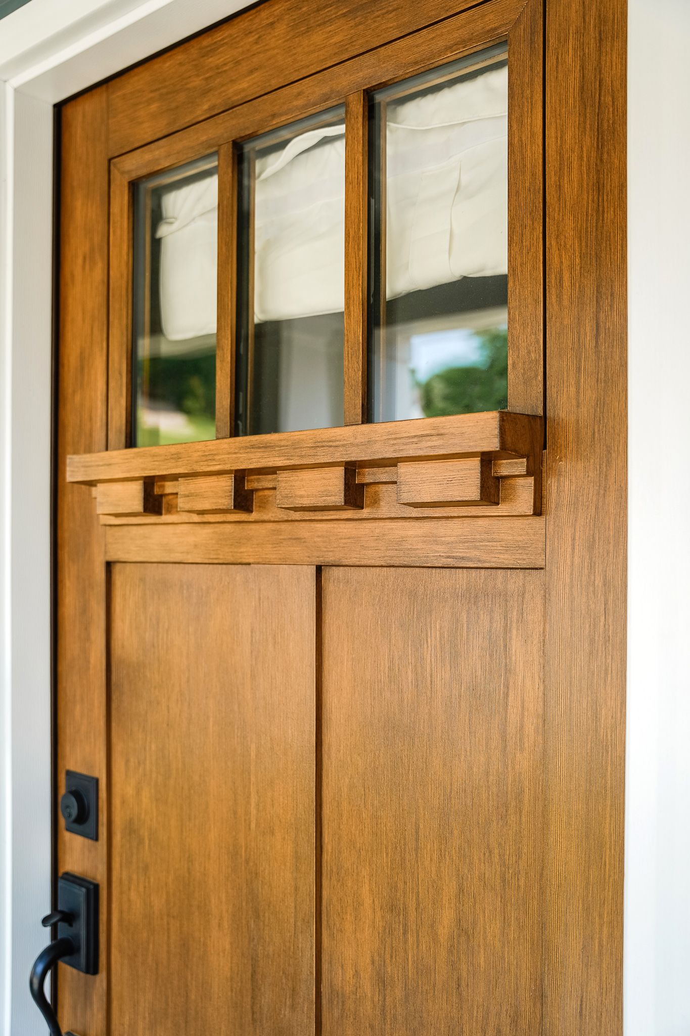 Craftsman-style fiberglass entry door detail with three-lite glass and dentil shelf